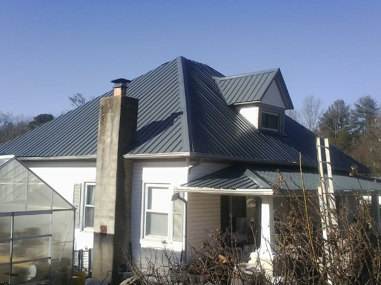 Dark blue standing seam metal roof on a white farmhouse with dormer — Slate & Tile Roof Repair by Roofing Brothers in Sigurd