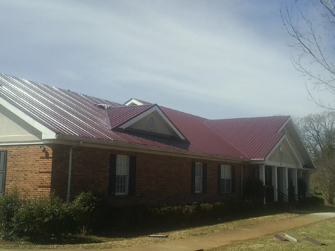 Red metal roof with gabled entries on a long brick building, from a Hail Damage Roof Repair job in Sigurd