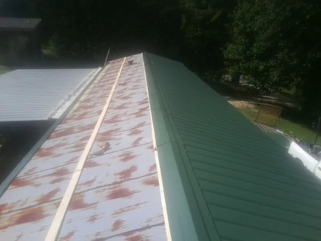 Old rusted panels beside newly installed green metal roofing — Wind Damage Roof Repair by Roofing Brothers in Sigurd