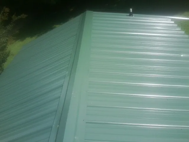 New green metal panels meeting at the ridge of a roof — Flat Roof Repair work by our crew in Sigurd