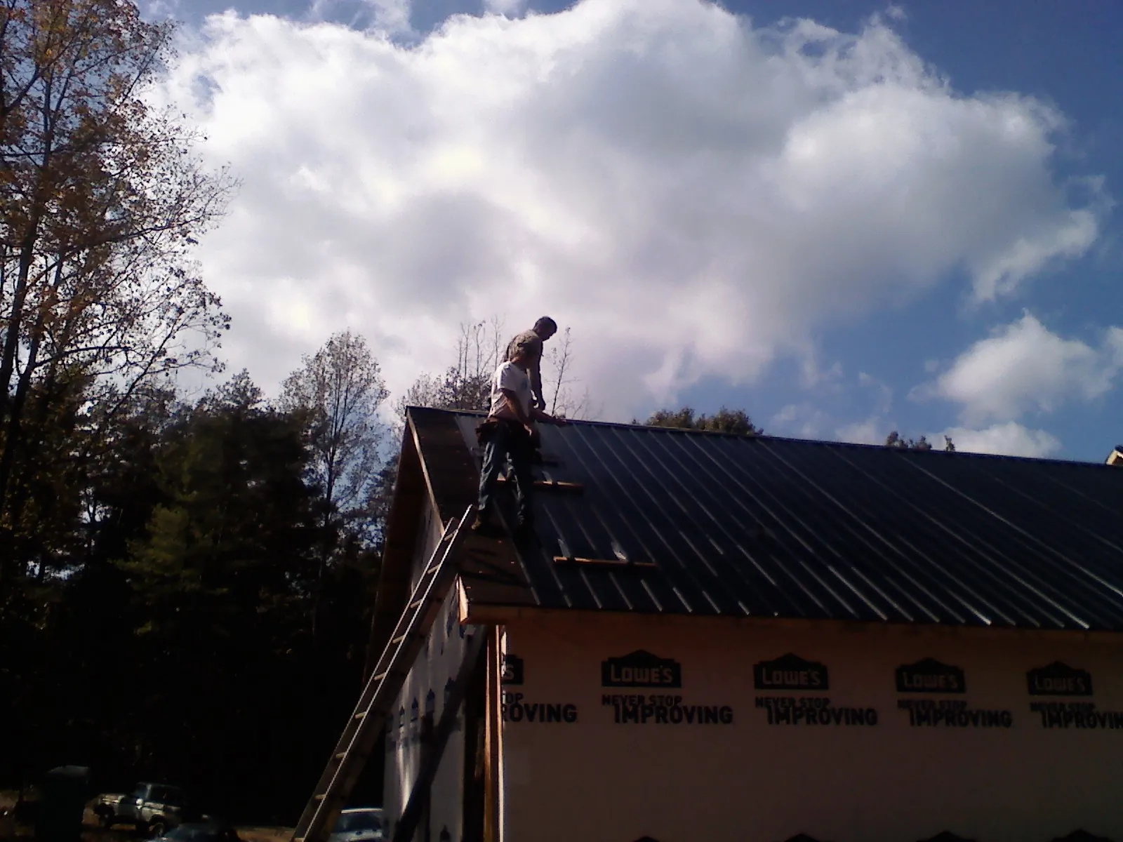 Roofer fastening dark metal panels high against a cloudy sky, from a Roof Inspection job in Sigurd